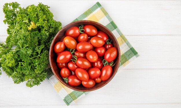 Vista superior de tomates em uma tigela com coentro chinês no pano e superfície de madeira com espaço de cópia