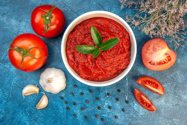 Vista superior de tomates frescos com pasta de tomate e alho na mesa azul