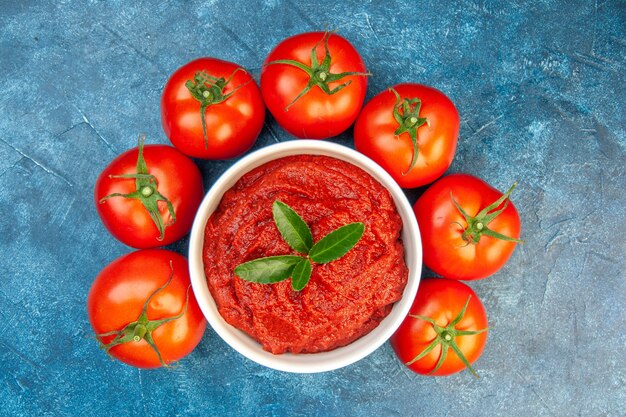 Vista superior de tomates frescos com pasta de tomate na mesa azul