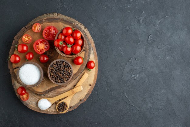 Vista superior de tomates frescos e especiarias na placa de madeira no lado direito na superfície preta