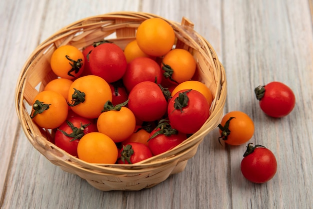 Vista superior de tomates frescos vermelhos e laranja doces em um balde em uma superfície de madeira cinza