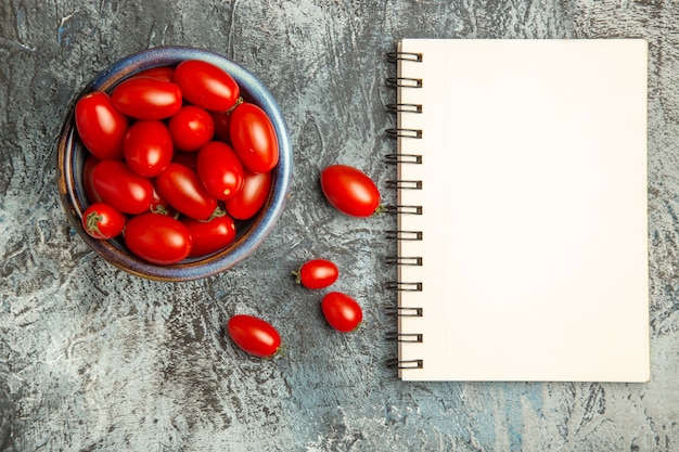 Vista superior de tomates vermelhos frescos com bloco de notas na mesa com luz escura, foto de frutas salada escura