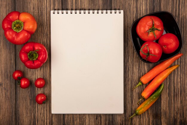 Vista superior de tomates vermelhos grandes em uma tigela com tomates cereja e pimentas isoladas em uma parede de madeira com espaço de cópia