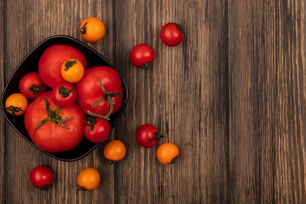 Vista superior de tomates vermelhos grandes em uma tigela com tomates cereja isolados em uma parede de madeira com espaço de cópia