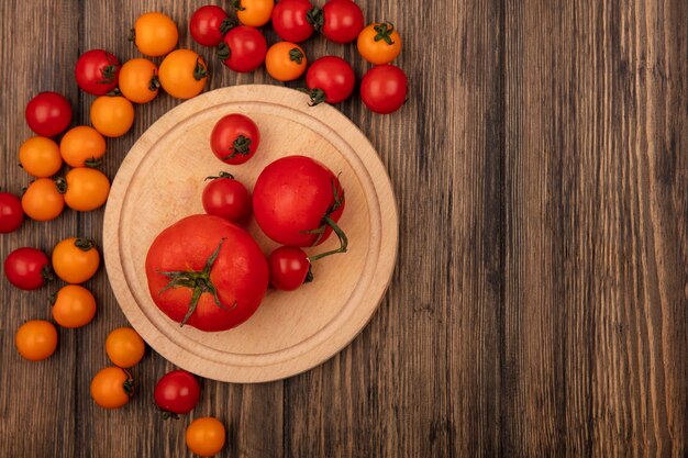 Vista superior de tomates vermelhos saudáveis em uma placa de cozinha de madeira com tomates cereja isolados em um fundo de madeira com espaço de cópia