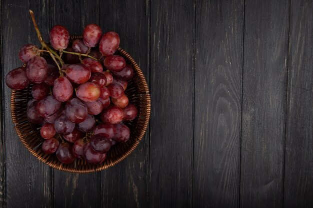 Vista superior de um cacho de uvas doces frescas em uma cesta de vime na mesa de madeira escura com espaço de cópia