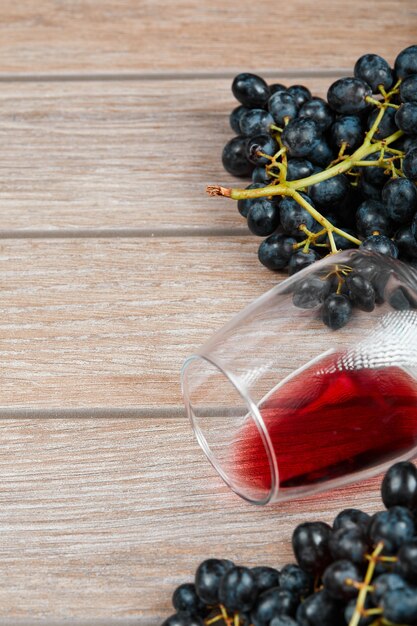 Vista superior de um cacho de uvas pretas e uma taça de vinho na superfície de madeira