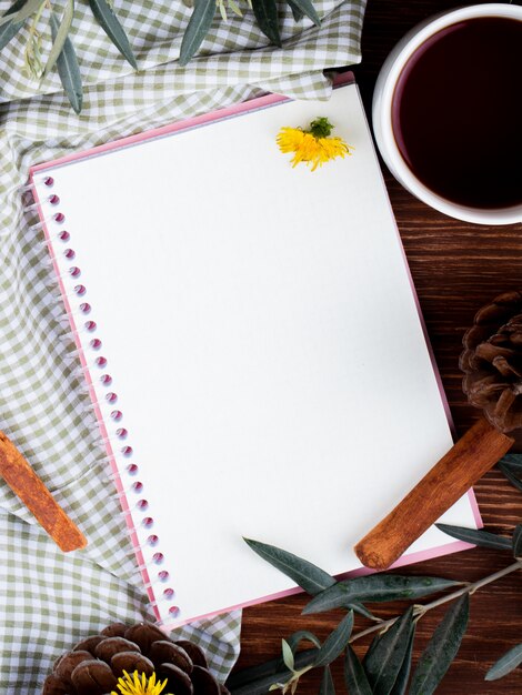 Vista superior de um caderno de desenho com uma caneca de chá e dentes de leão espalhados na madeira