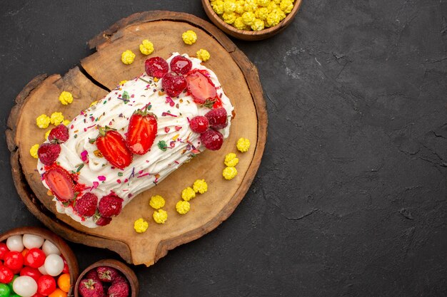 Vista superior de um delicioso bolo de creme com frutas e doces no escuro