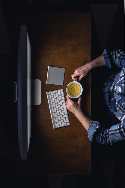 Foto grátis vista superior de um homem trabalhando no computador à noite segurando uma xícara de chá