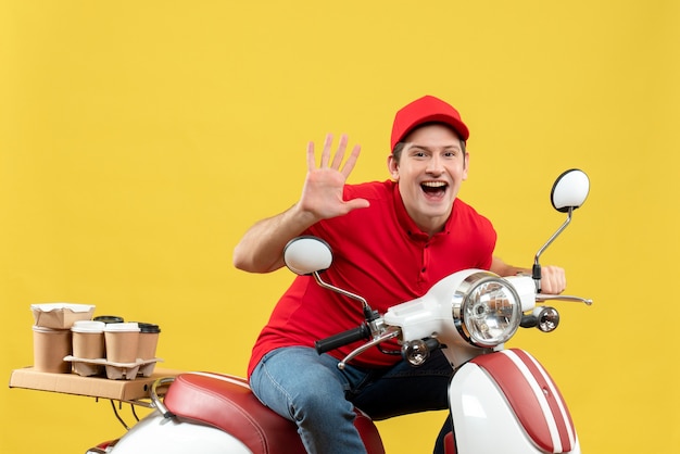 Foto grátis vista superior de um jovem adulto sorridente usando blusa vermelha e chapéu, entregando pedidos, mostrando cinco na parede amarela