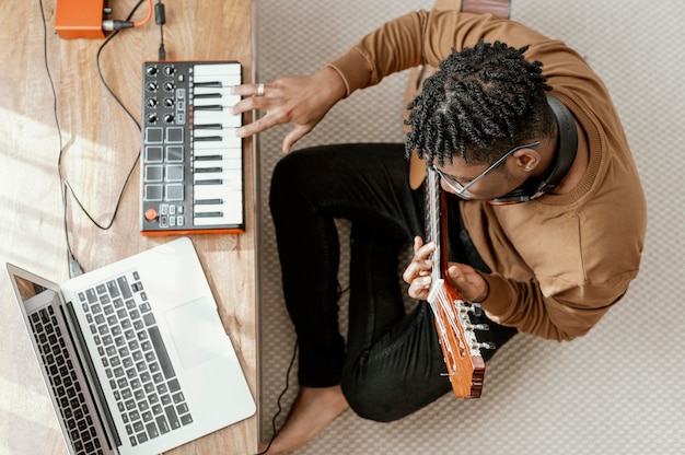 Vista superior de um músico masculino em casa tocando violão e mixando com o laptop