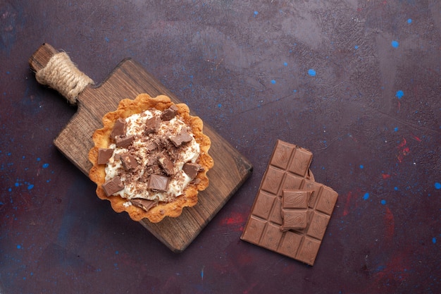 Vista superior de um pequeno bolo cremoso com pedaços de chocolate e barras na superfície escura