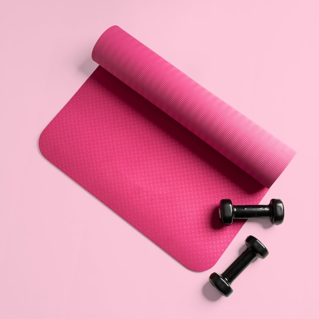 Vista superior de um tapete rosa de fitness e dois halteres pretos isolados em uma superfície rosa