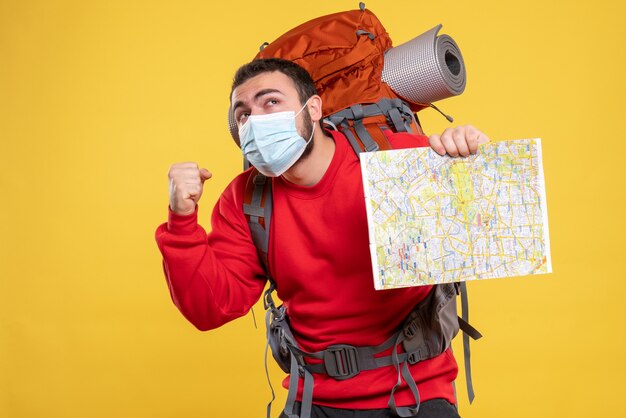 Vista superior de um viajante com pensamento emocional usando uma máscara médica com uma mochila segurando um mapa sobre fundo amarelo