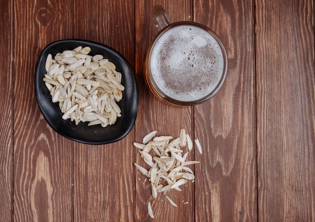 Vista superior de uma caneca de cerveja e uma garrafa de cerveja com lanche salgado sementes de girassol em uma tigela de madeira rústica