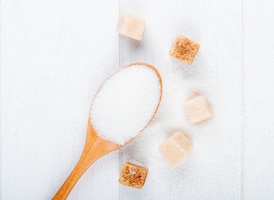 Foto grátis vista superior de uma colher de pau com açúcar branco e açúcar em pó no fundo branco