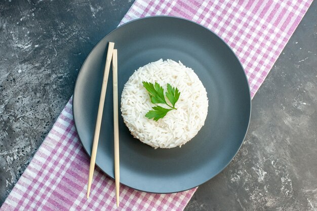 Vista superior de uma deliciosa refeição de arroz servida com verde e pauzinhos em uma placa preta em uma toalha roxa despojada sobre fundo escuro