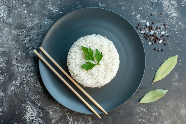 Vista superior de uma deliciosa refeição de arroz servida com verde e pauzinhos em uma placa preta. folhas de pimentão em fundo escuro