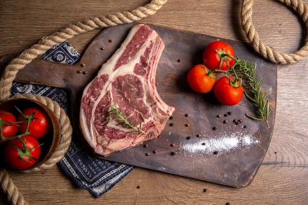 Vista superior de uma fatia de carne crua com tomates vermelhos frescos na foto de madeira crua de refeição