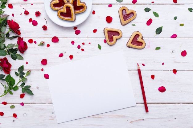Foto grátis vista superior de uma folha de papel em branco sobre uma mesa de madeira com biscoitos e rosas