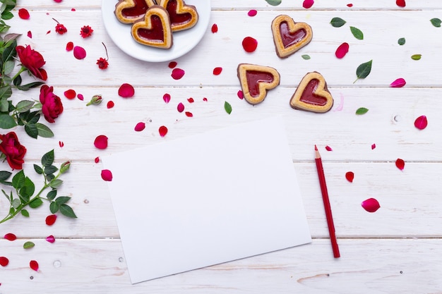 Vista superior de uma folha de papel em branco sobre uma mesa de madeira com biscoitos e rosas