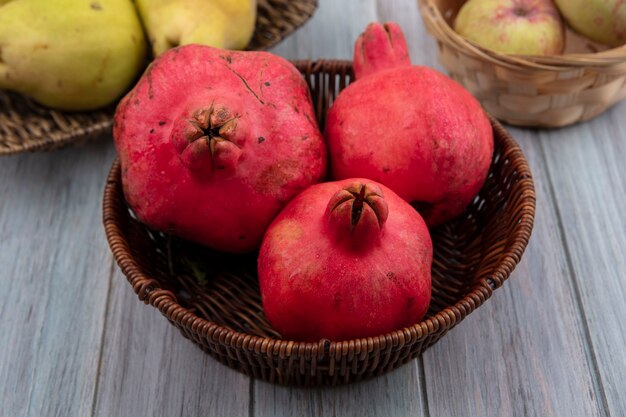 Vista superior de uma fruta redonda com uma casca de couro vermelho romãs em um balde com maçãs e marmelos em um fundo cinza