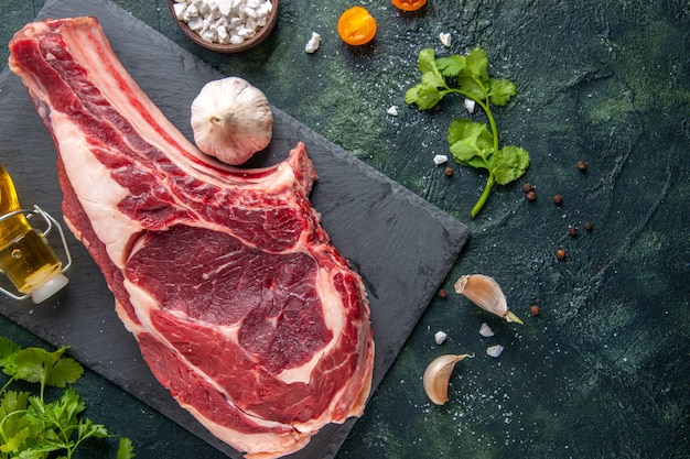 Vista superior de uma grande fatia de carne crua com verduras na superfície escura