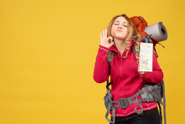 Foto grátis vista superior de uma jovem garota viajando com máscara médica, recolhendo sua bagagem e segurando o mapa, fazendo um gesto de óculos