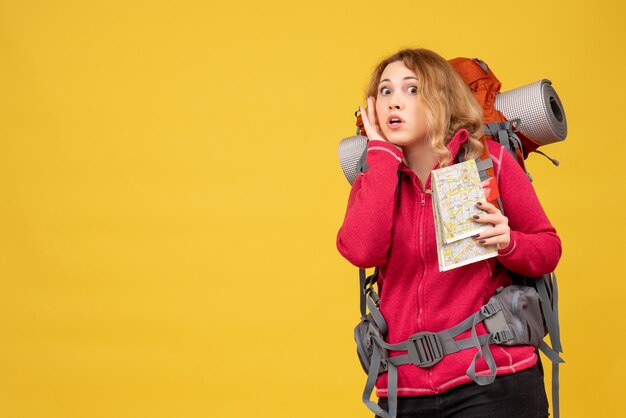 Vista superior de uma jovem garota viajando com máscara médica, recolhendo sua bagagem e segurando um mapa, ouvindo as últimas fofocas