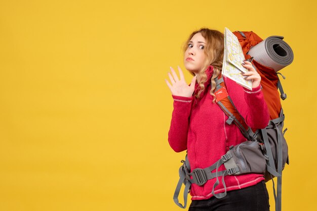 Vista superior de uma jovem incerta e insegura, viajando com máscara médica, recolhendo sua bagagem e segurando o mapa