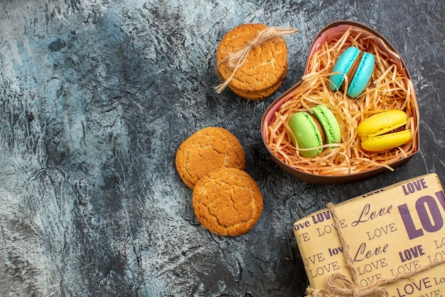 Vista superior de uma linda caixa de presente com macarons e biscoitos no lado esquerdo em um fundo escuro de gelo