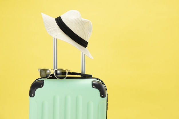 Vista superior de uma mala, óculos de sol, câmera e chapéu em um fundo amarelo - conceito de férias