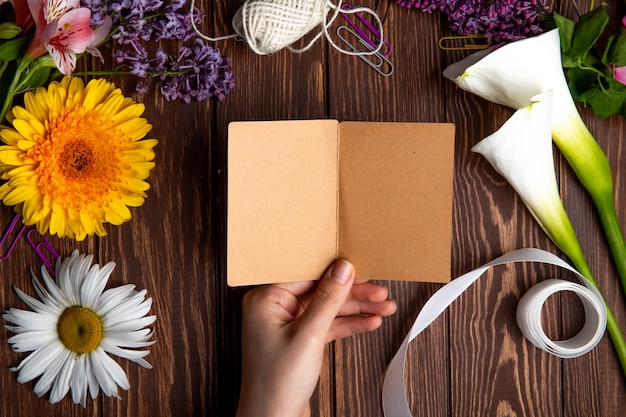 Vista superior de uma mão com um cartão postal e gerbera com margarida flores sobre fundo de madeira