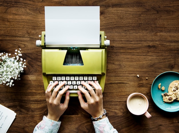 Vista superior de uma mulher digitando em um papel em branco de uma máquina de escrever retrô