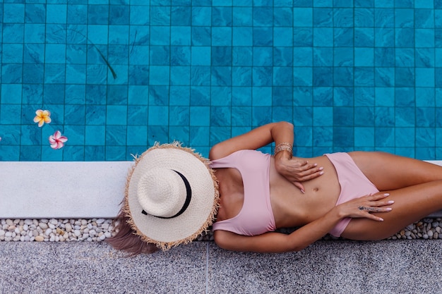 Vista superior de uma mulher magra de biquíni à beira da piscina aproveitando as férias