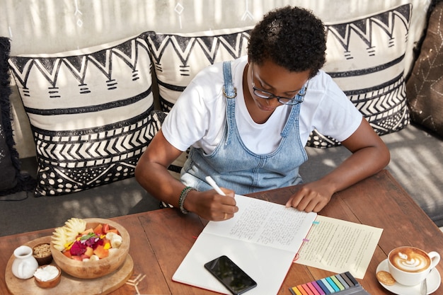 Vista superior de uma mulher negra elegante e atraente escreve resenha de livro no bloco de notas