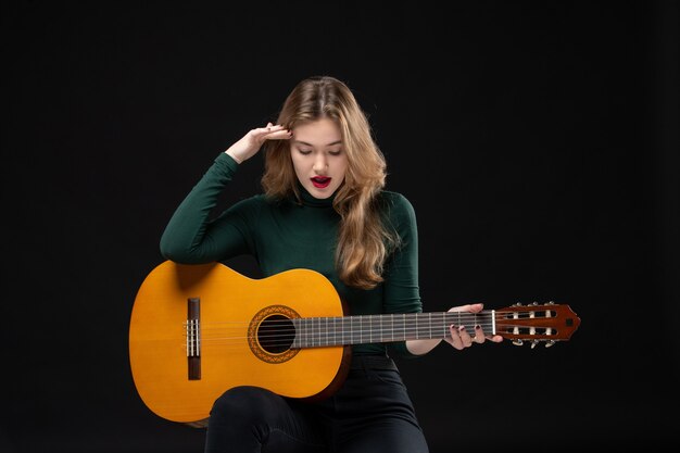 Vista superior de uma musicista segurando uma guitarra e olhando para baixo no preto