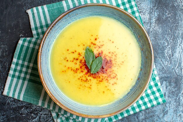 Vista superior de uma panela azul com sopa saborosa servida com hortelã em uma toalha verde despojada sobre fundo azul