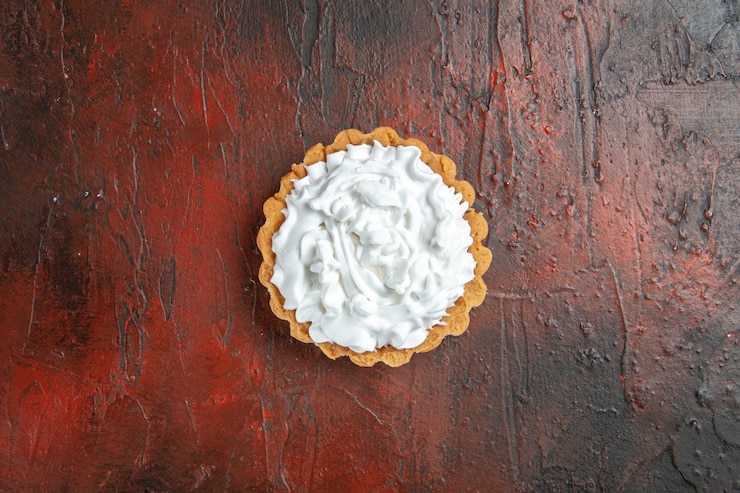 Foto grátis vista superior de uma pequena torta com creme de confeitaria na superfície vermelha escura