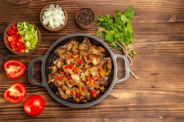 Vista superior de uma refeição de vegetais cozidos com carne e pimentão fresco fatiado em uma mesa de madeira marrom