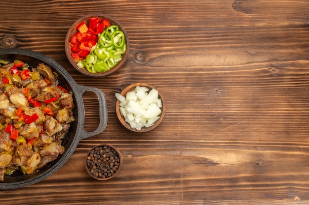 Vista superior de uma refeição de vegetais cozidos com carne e pimentão fresco fatiado em uma mesa de madeira marrom