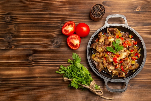 Vista superior de uma refeição de vegetais cozidos com carne e verduras em uma mesa de madeira marrom