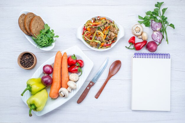 Vista superior de uma salada de legumes fresca fatiada com carne, junto com pães e vegetais inteiros e verdes na luz, salada de refeição de vegetais