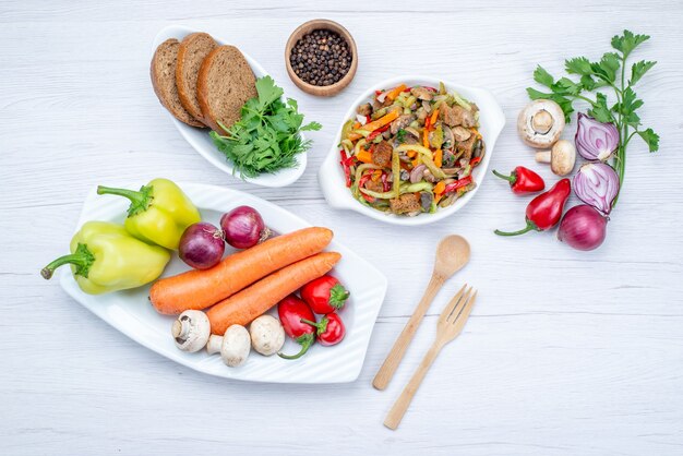 Vista superior de uma salada de legumes fresca fatiada junto com pães, vegetais inteiros e verduras em uma mesa leve, salada de comida de vegetais