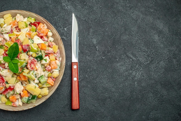 Vista superior de uma tigela de salada de legumes com faca em fundo cinza escuro