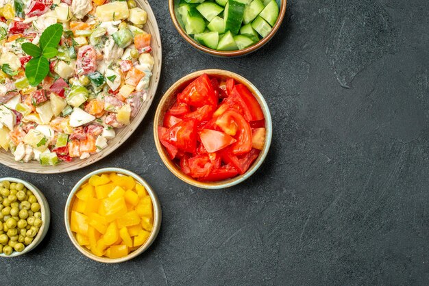 Vista superior de uma tigela de salada de legumes com tigelas de legumes ao lado em fundo verde escuro