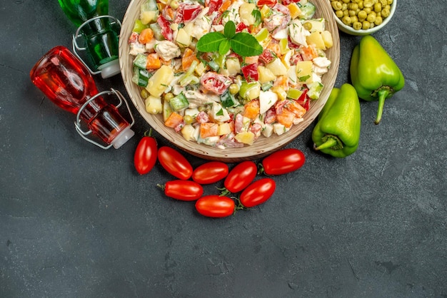 Foto grátis vista superior de uma tigela de salada de vegetais com garrafas de vinagre de óleo em fundo cinza escuro