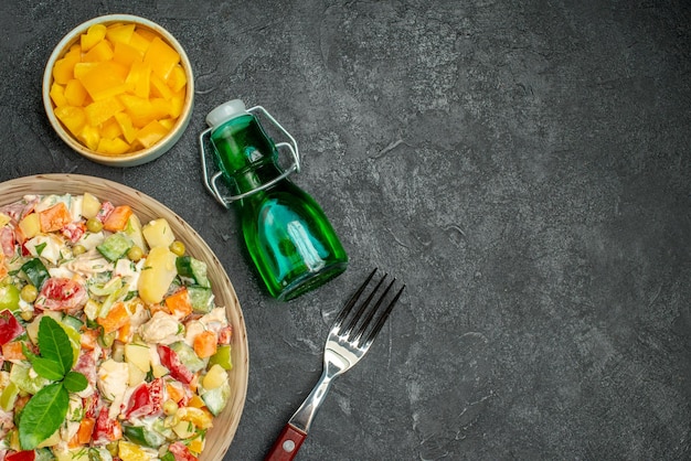 Vista superior de uma tigela de salada vegetariana com um garfo de pimentão cortado e garrafa de óleo em fundo escuro