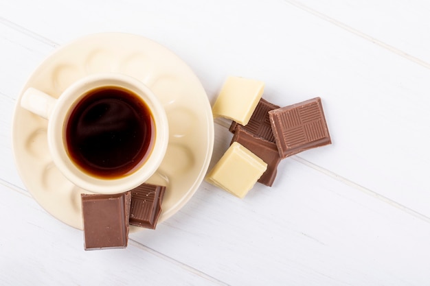 Vista superior de uma xícara de café com chocolate branco e escuro sobre fundo branco de madeira